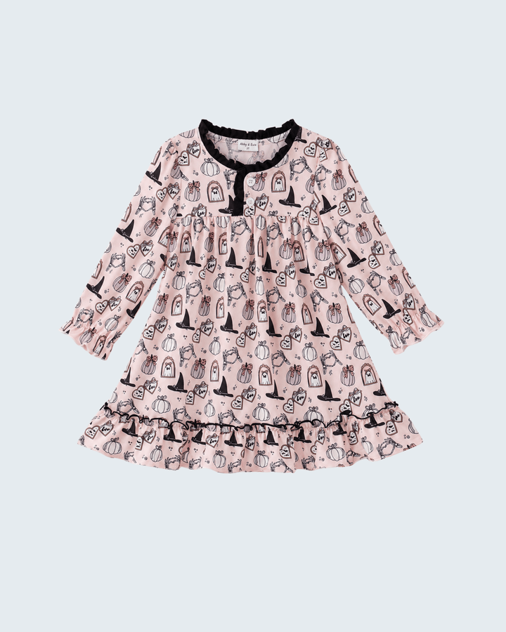 A long-sleeve baby dress in light pink with a black and white pumpkin print, featuring a ruffled hem and neckline with black trim, shown against a light gray background.