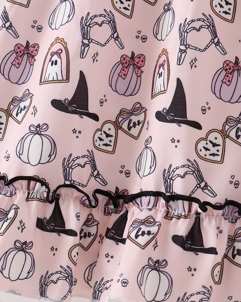 A close-up of a light pink fabric with a Halloween print featuring black witch hats, white pumpkins, ghosts, bats, and bones, finished with a black ruffled trim.