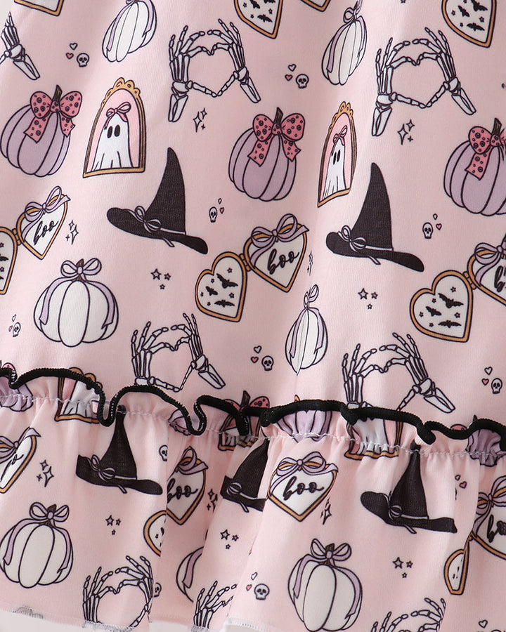 A close-up of a light pink fabric with a Halloween print featuring black witch hats, white pumpkins, ghosts, bats, and bones, finished with a black ruffled trim.