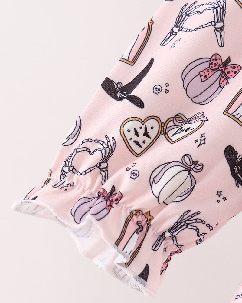 A close-up of a light pink fabric with a whimsical Halloween-themed print featuring pumpkins, skeletons, a witch&