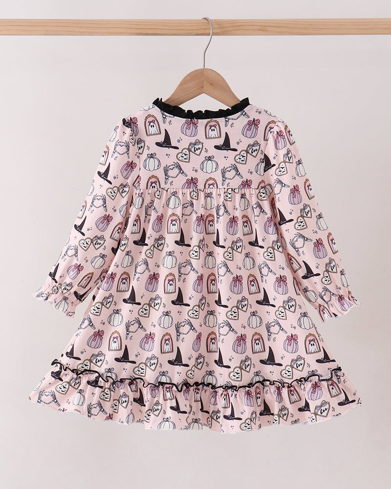 A pink long-sleeve dress with a black ruffled collar and an all-over print of cartoon pumpkins and witch hats, hanging on a wooden hanger against a plain light gray wall.