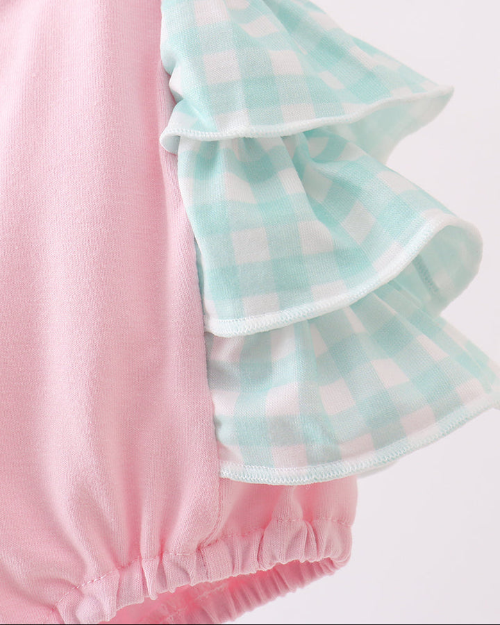Pink and green baby romper with ruffled details on a light gray background