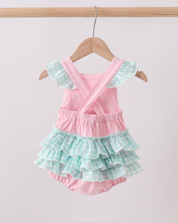 Pink and green ruffled baby romper on a wooden hanger against a light pink background