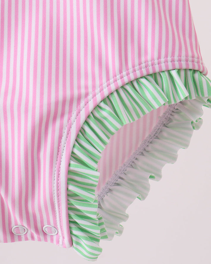 Pink and green striped swimsuit with ruffled bottom on a light pink background