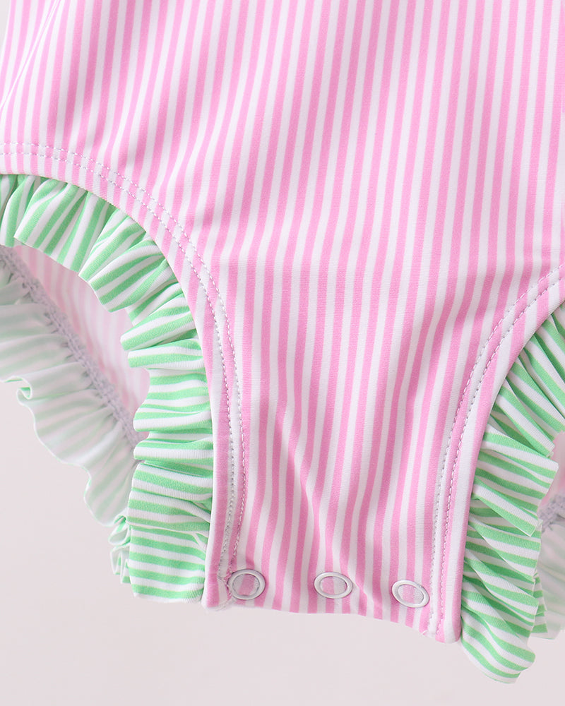 Pink and green striped swimsuit with ruffled edges on a light pink background