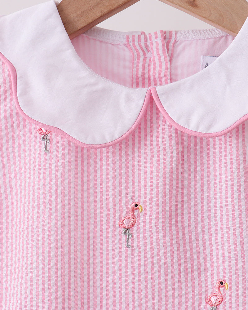 Pink checkered dress with white collar and embroidered flamingos on a wooden hanger.