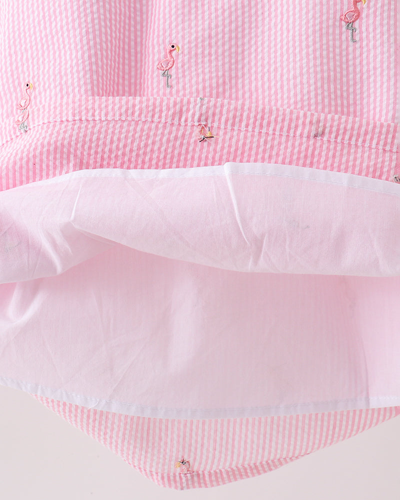 Close-up of a pink fabric with small embroidered flamingo designs on a white background