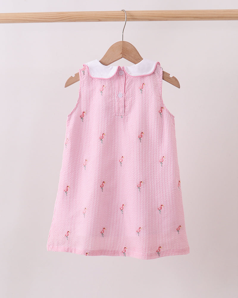 Pink dress with white collar on a wooden hanger against a light pink background