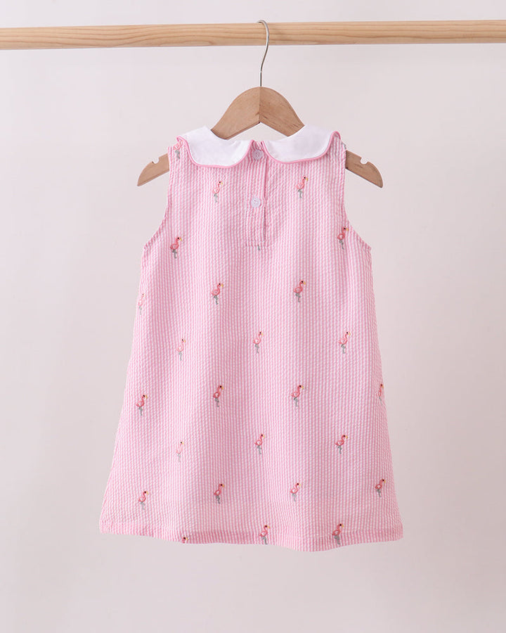 Pink dress with white collar on a wooden hanger against a light pink background