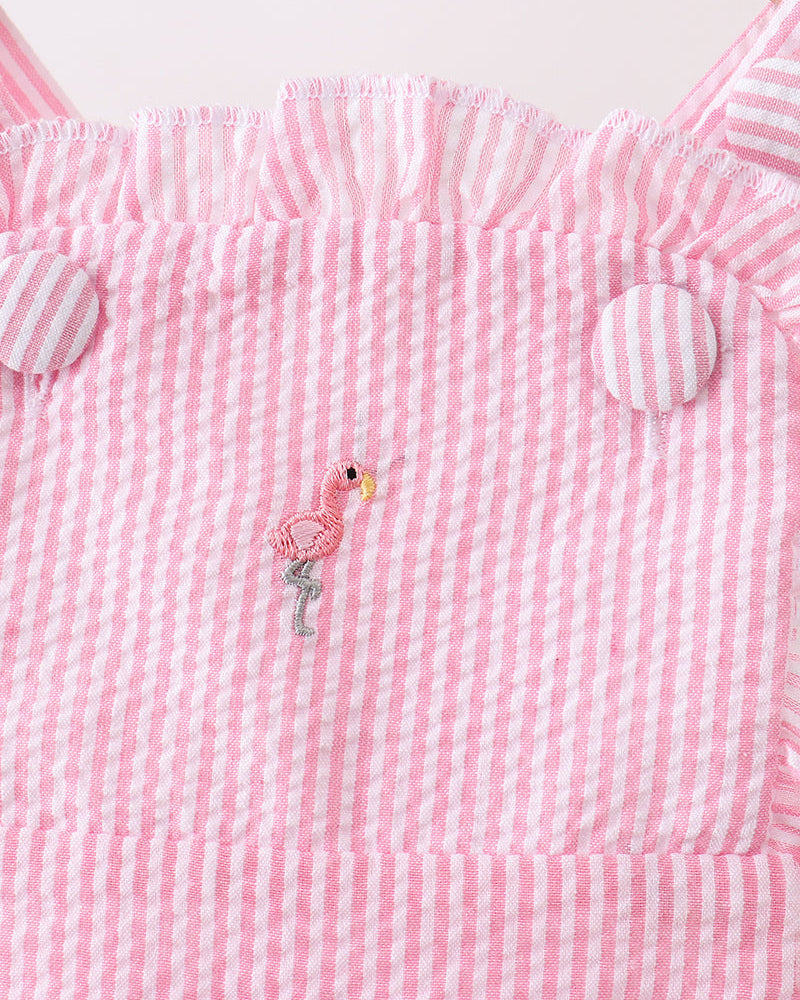 Pink and white striped romper with a flamingo design on a wooden surface