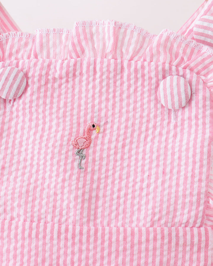 Pink and white striped romper with a flamingo design on a wooden surface