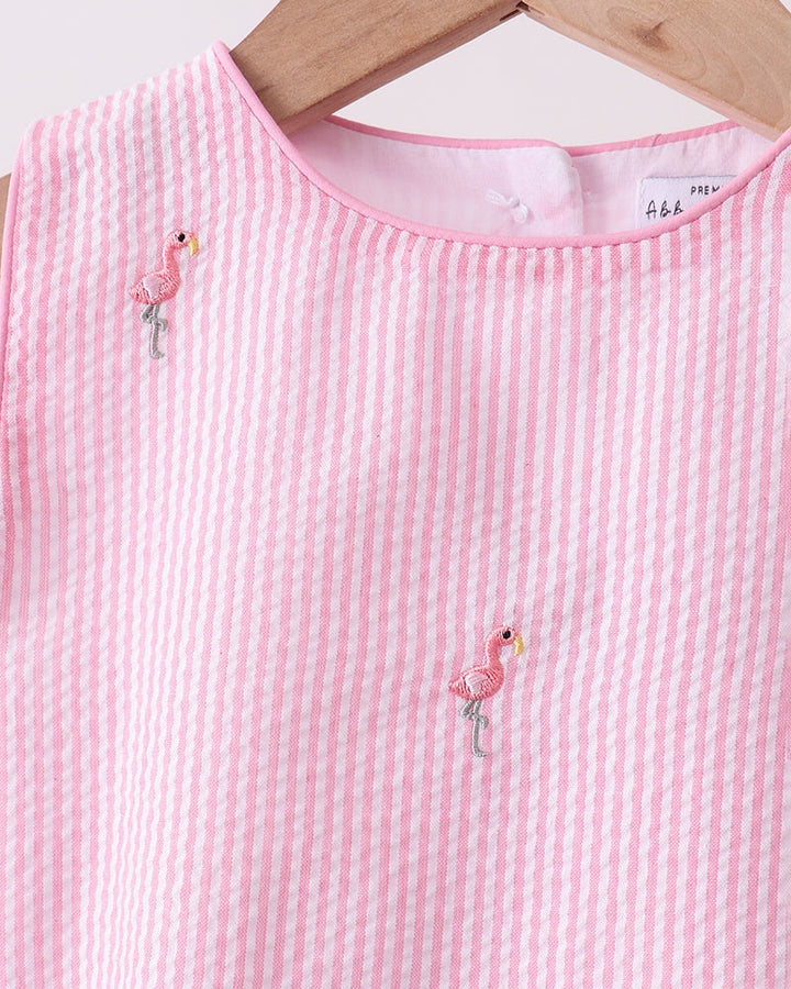 Pink textured fabric with embroidered flamingo design on a hanger
