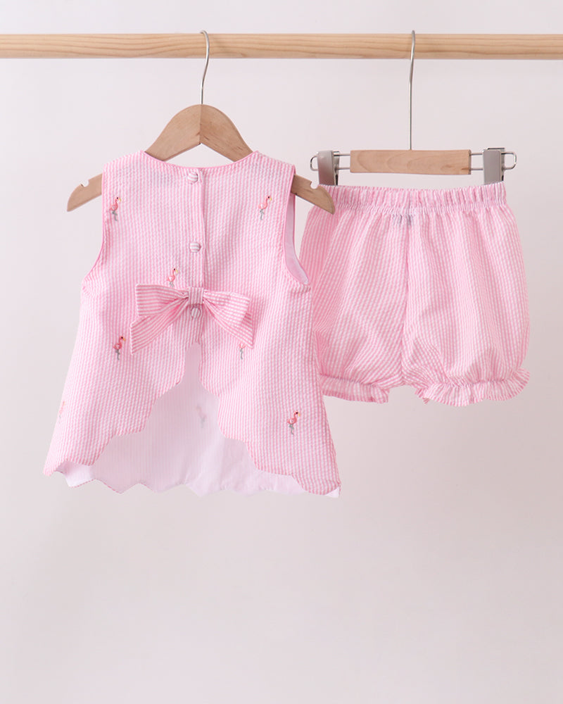 Pink baby outfit with top and bloomers on hangers against a light pink background