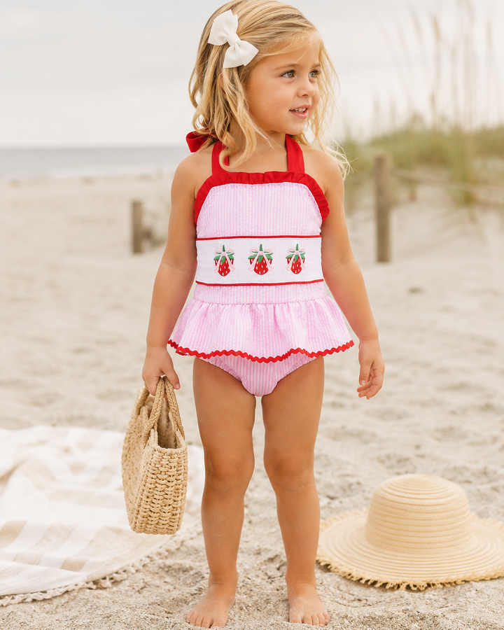 Young girl in a pink and red swimsuit standing on a sandy beach.