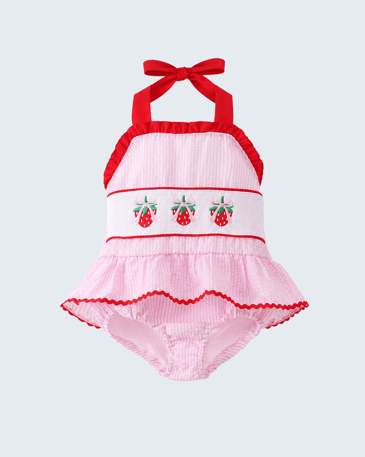Pink baby swimsuit with red accents and cherry design on a light gray background