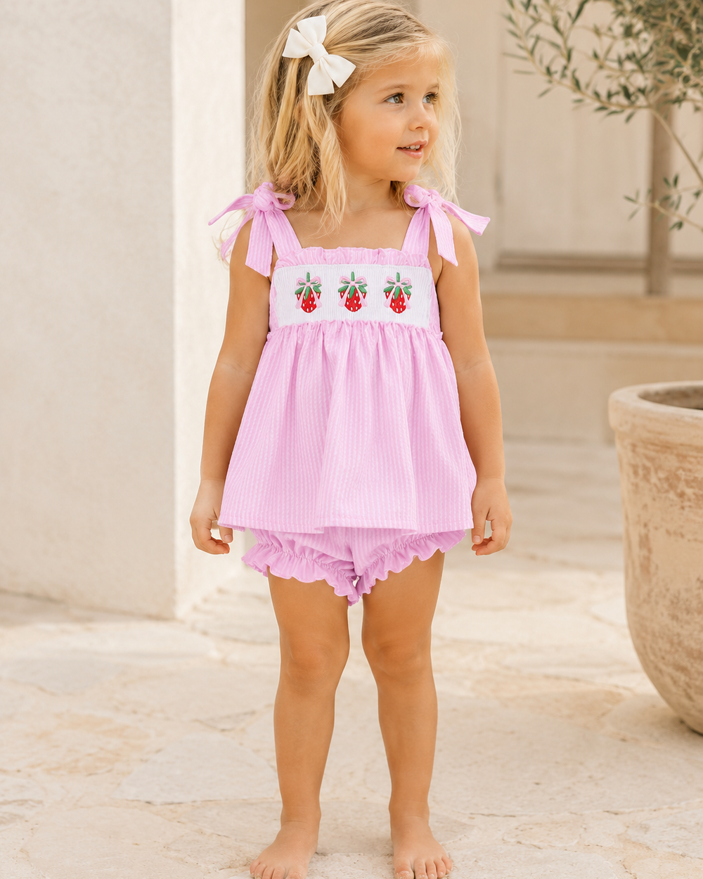Young girl wearing a pink outfit with strawberry design outdoors.