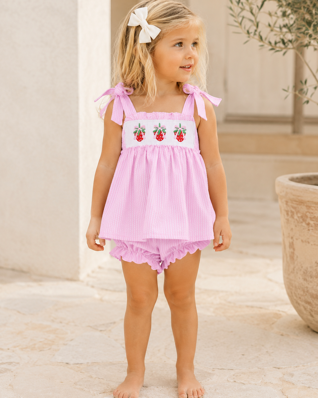 Young girl wearing a pink outfit with strawberry design outdoors.