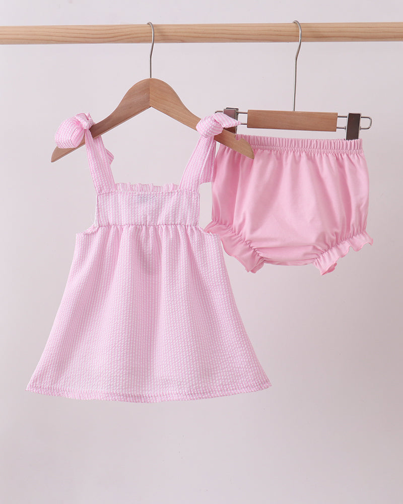 Pink baby dress and bloomers on hangers against a light gray background