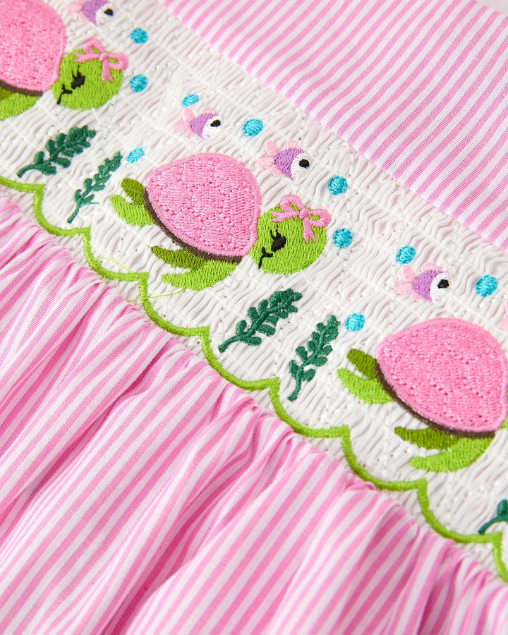 Pink fabric with embroidered green turtles and pink flowers on a white border against a pink striped background.