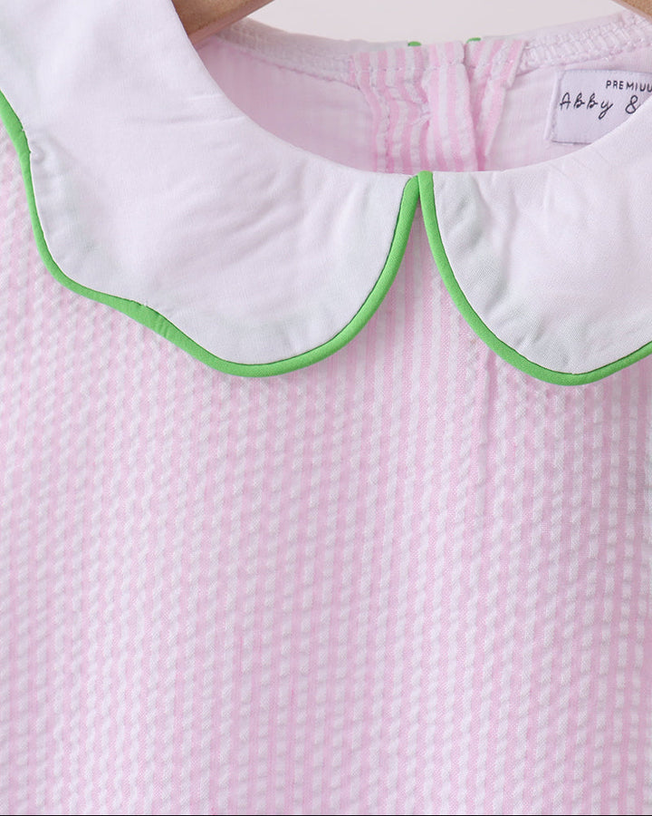 Close-up of a pink textured fabric with a white collar and green trim on a hanger.