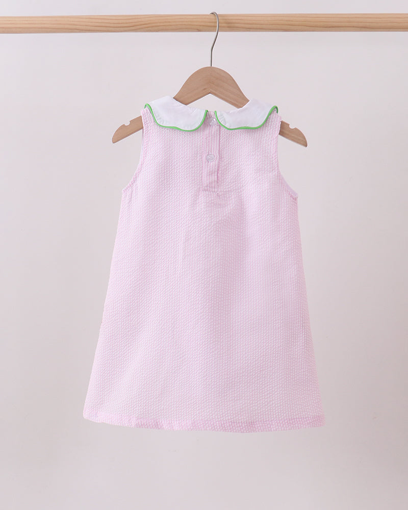 Pink dress with white collar on a wooden hanger against a light background