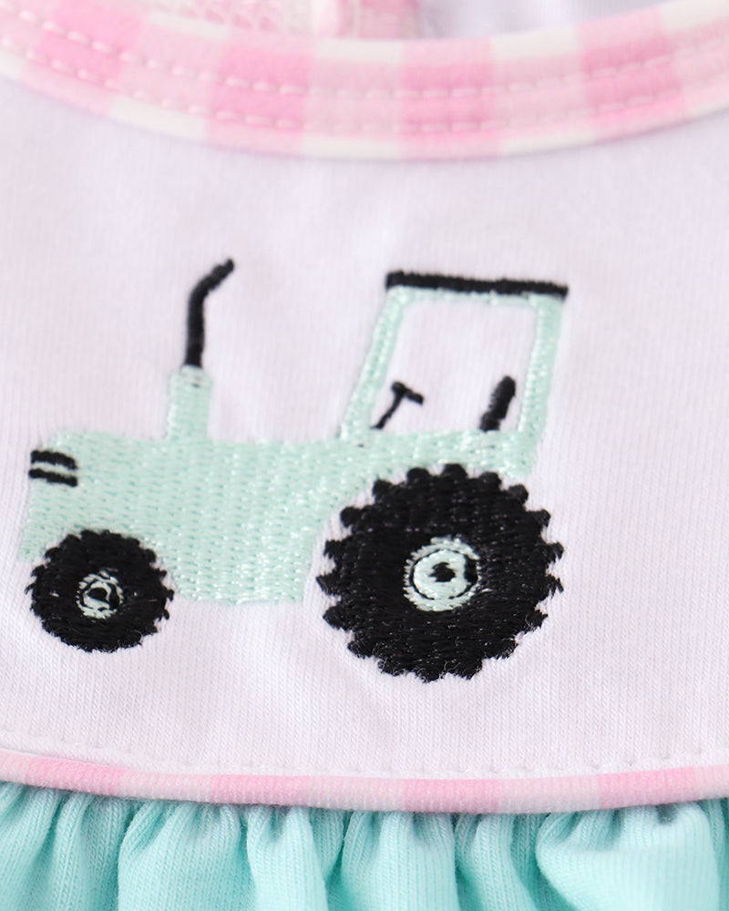 Close-up of a dress with a embroidered green tractor design on a light blue background.