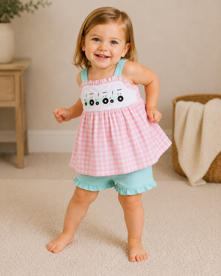 Child wearing a pink checkered dress with a white top and blue shorts indoors.