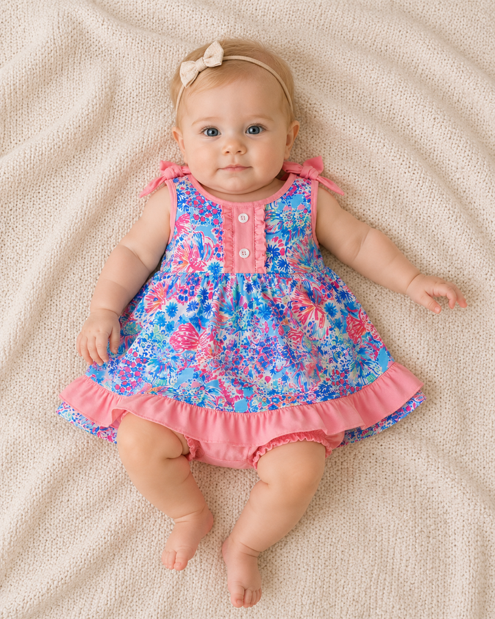 Baby wearing a colorful floral dress lying on a beige blanket