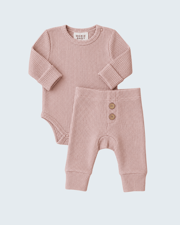 A two-piece baby clothing set from Mickle Baby, featuring a long-sleeve ribbed bodysuit and matching harem pants in a dusty rose pink color, laid flat against a light gray background.