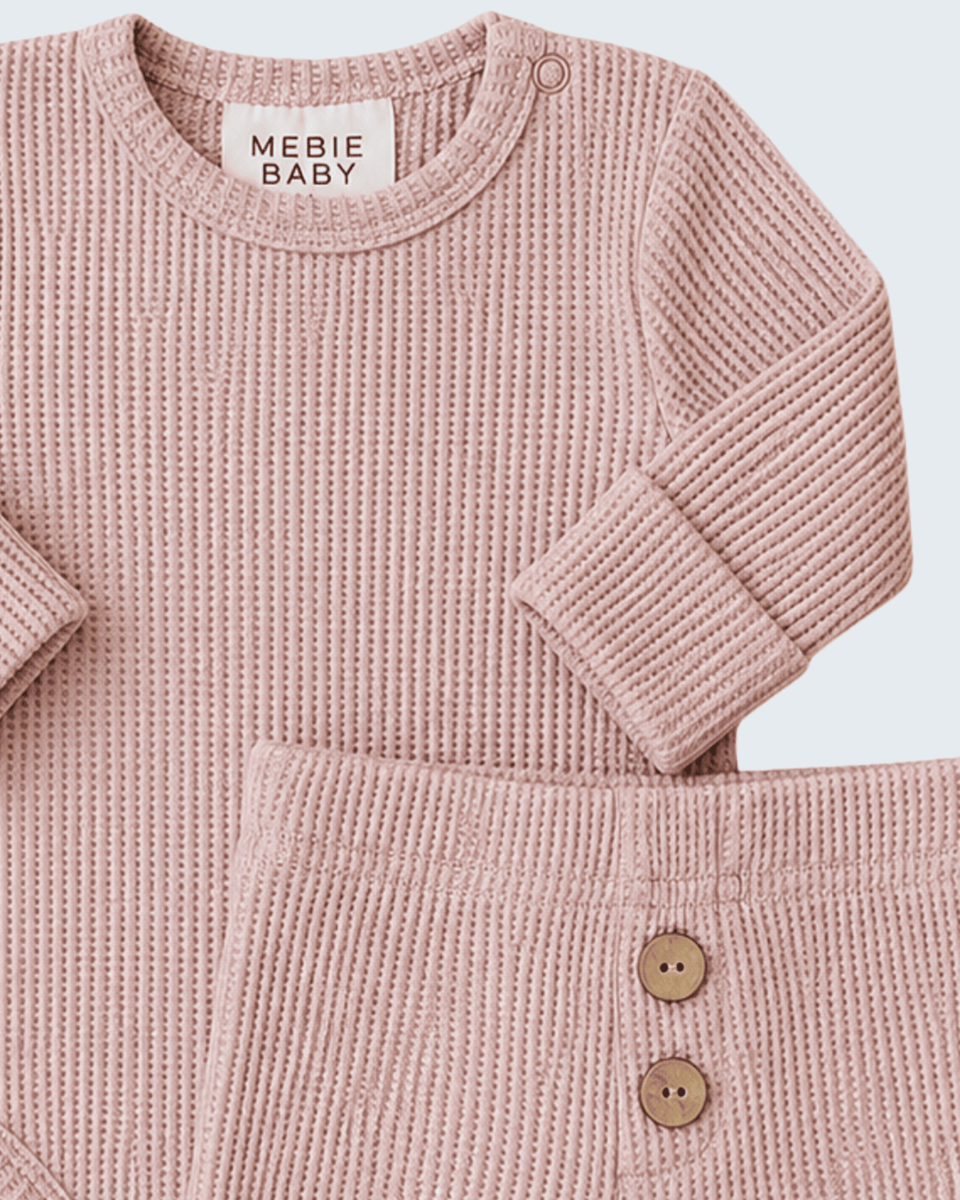 A close-up of a baby knit two-piece outfit in dusty pink, featuring a long-sleeve crewneck top and matching pants with two wooden buttons, from the brand MEBIE BABY.