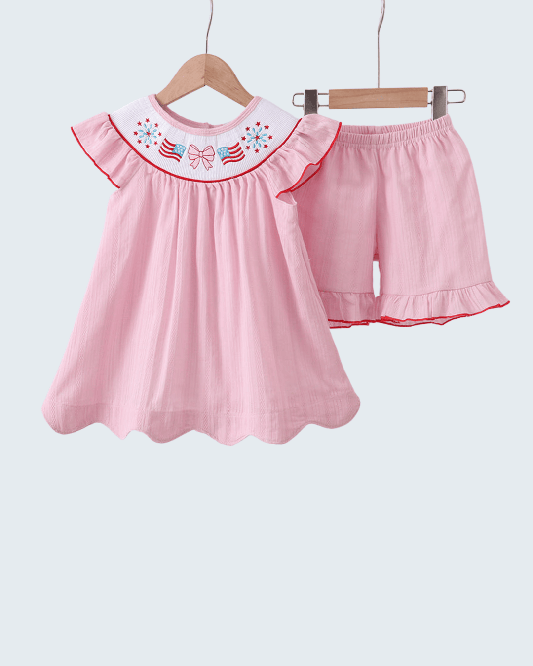 Pink children's outfit with top and shorts on hangers against a white background