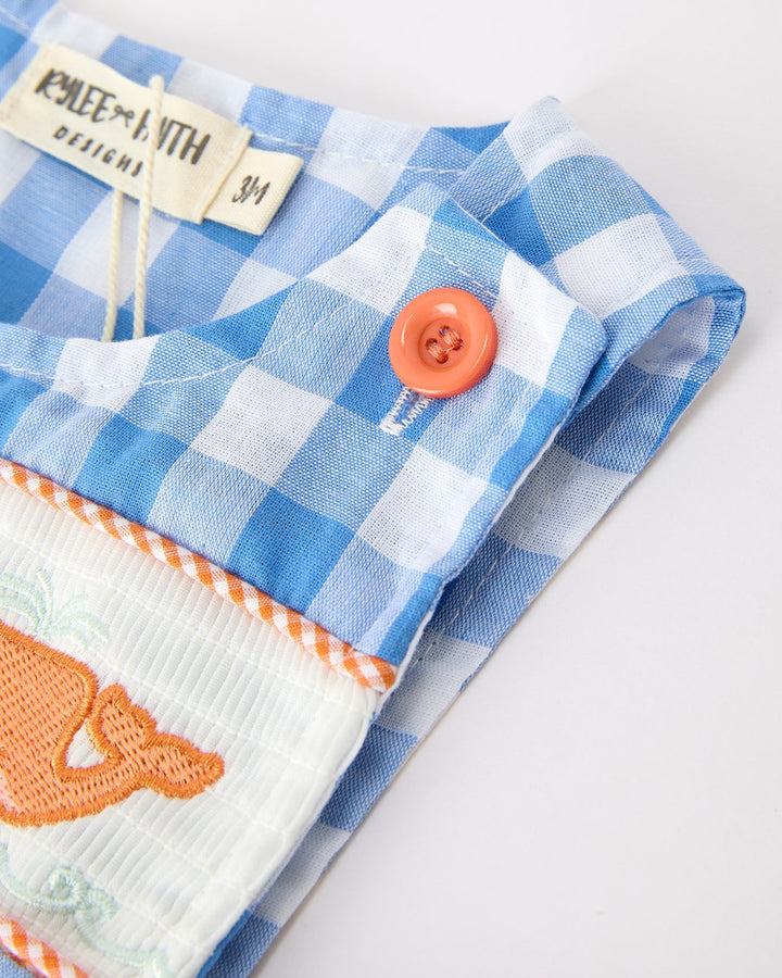Folded blue and white checkered fabric with an orange button and embroidered design on a light background