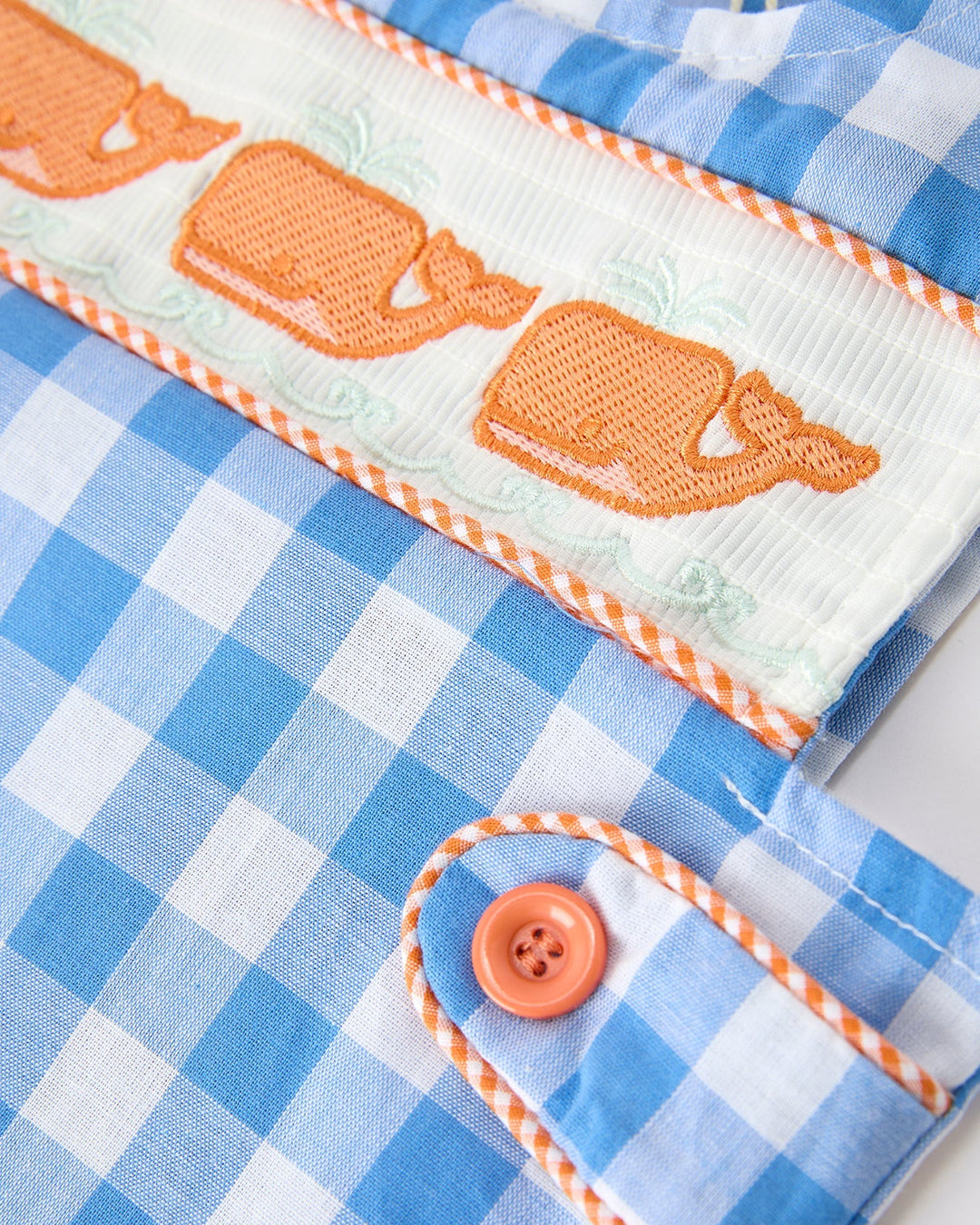 Close-up of a blue checkered fabric with orange accents and a button.