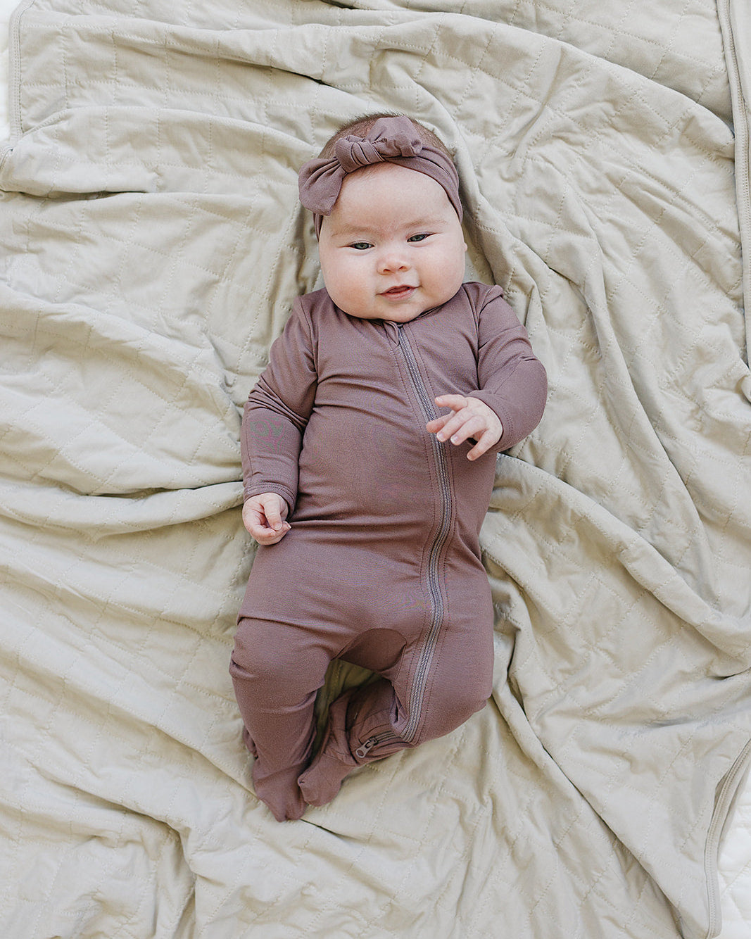 Baby in a brown outfit and headband lying on beige fabric