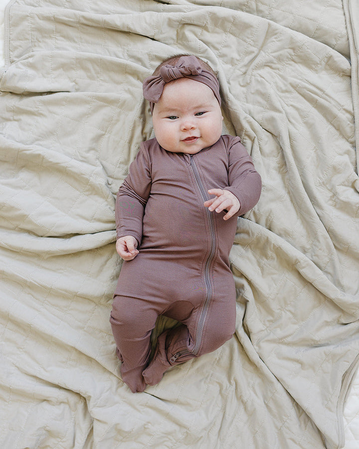 Baby in a brown outfit and headband lying on beige fabric