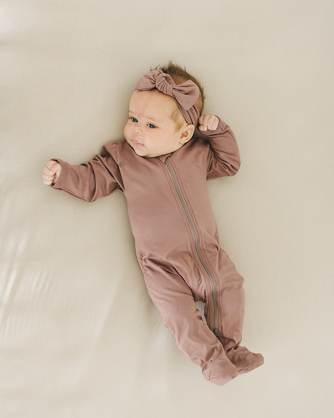 Baby in a brown onesie with a bow on a beige surface