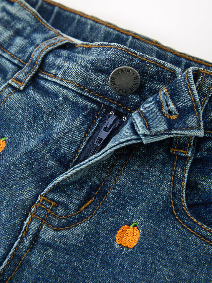 Denim jeans close-up: waistband tag, button, and orange pumpkin embroidery