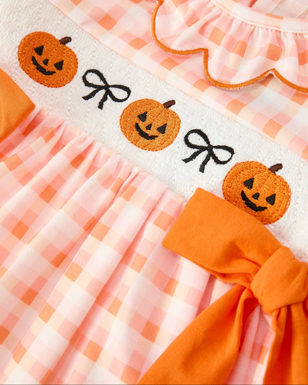 Plush pumpkin applique waistband with orange ribbon bow on girls plaid dress