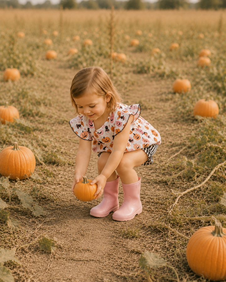 Child wearing pumpkin print ruffle top and black-and-white checkered bloomers