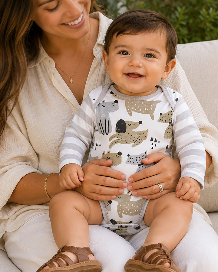 Woman holding a baby wearing a onesie with animal patterns outdoors.