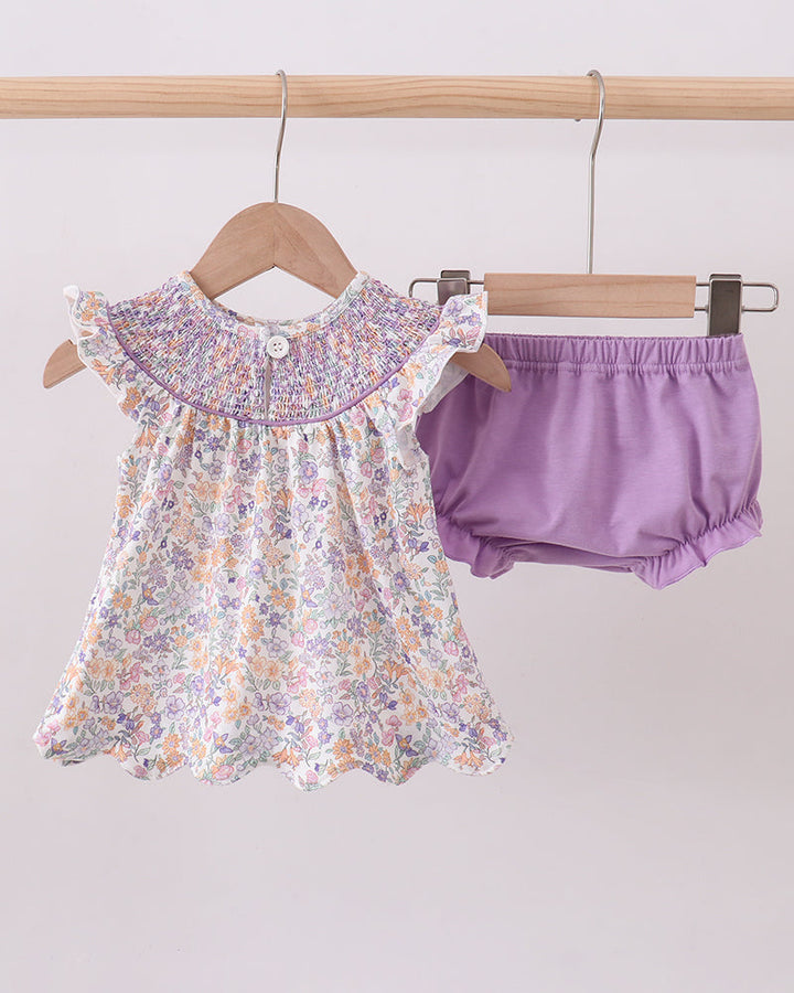 Floral dress and purple bloomers hanging on a wooden rack against a light gray background