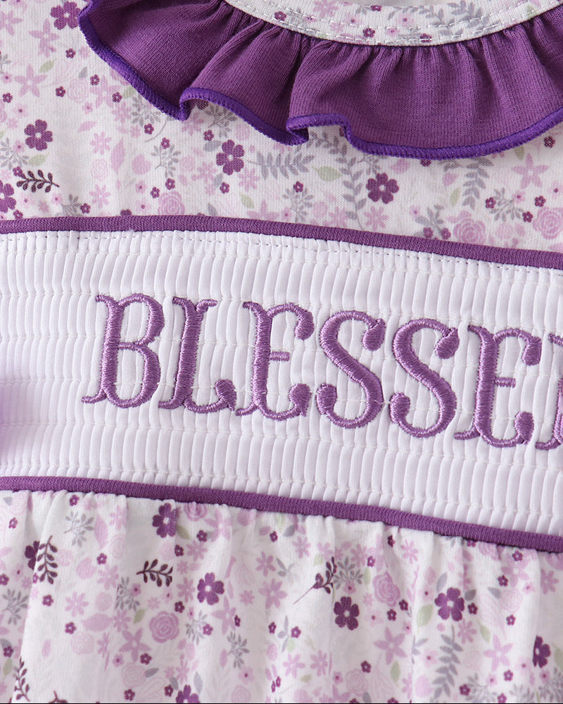 Close-up of a baby dress with a purple ruffled collar, a white smocked band embroidered with &