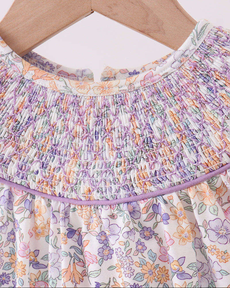 Floral dress with smocked neckline on a wooden hanger against a white background