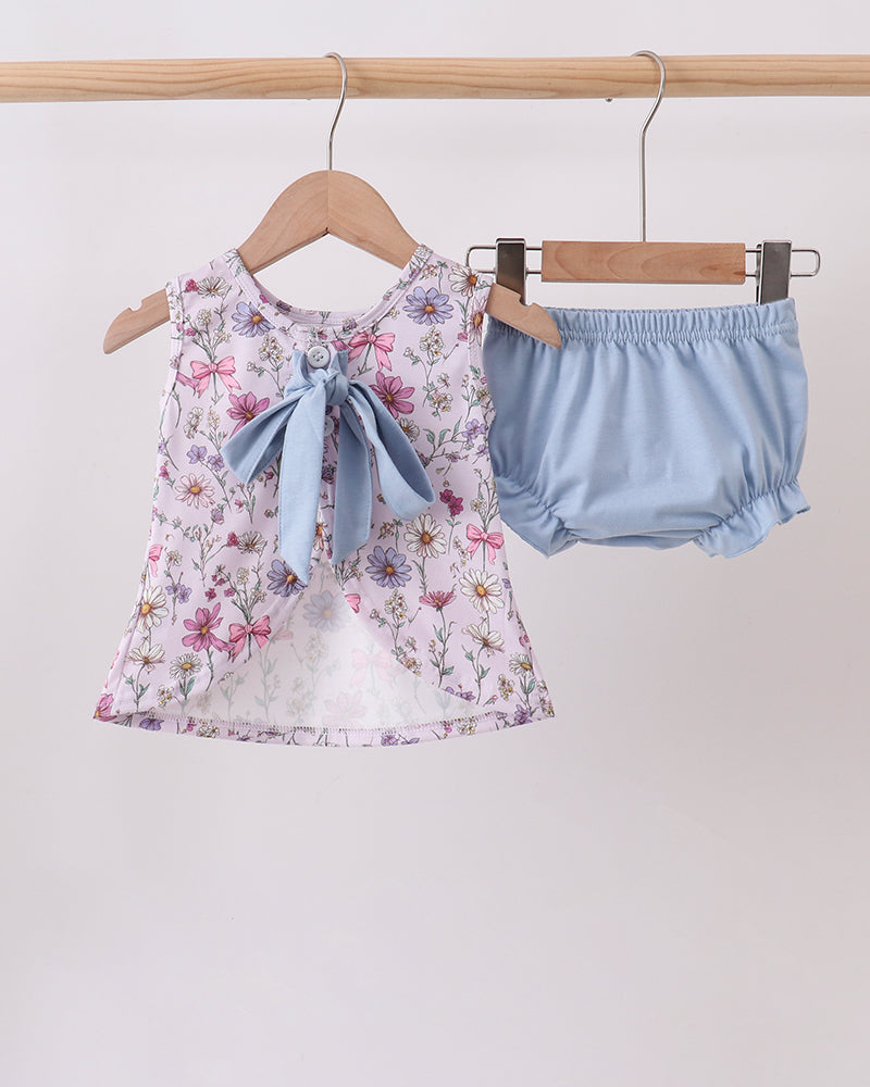 Floral top with a bow and light blue bloomers hanging on a rack against a white background