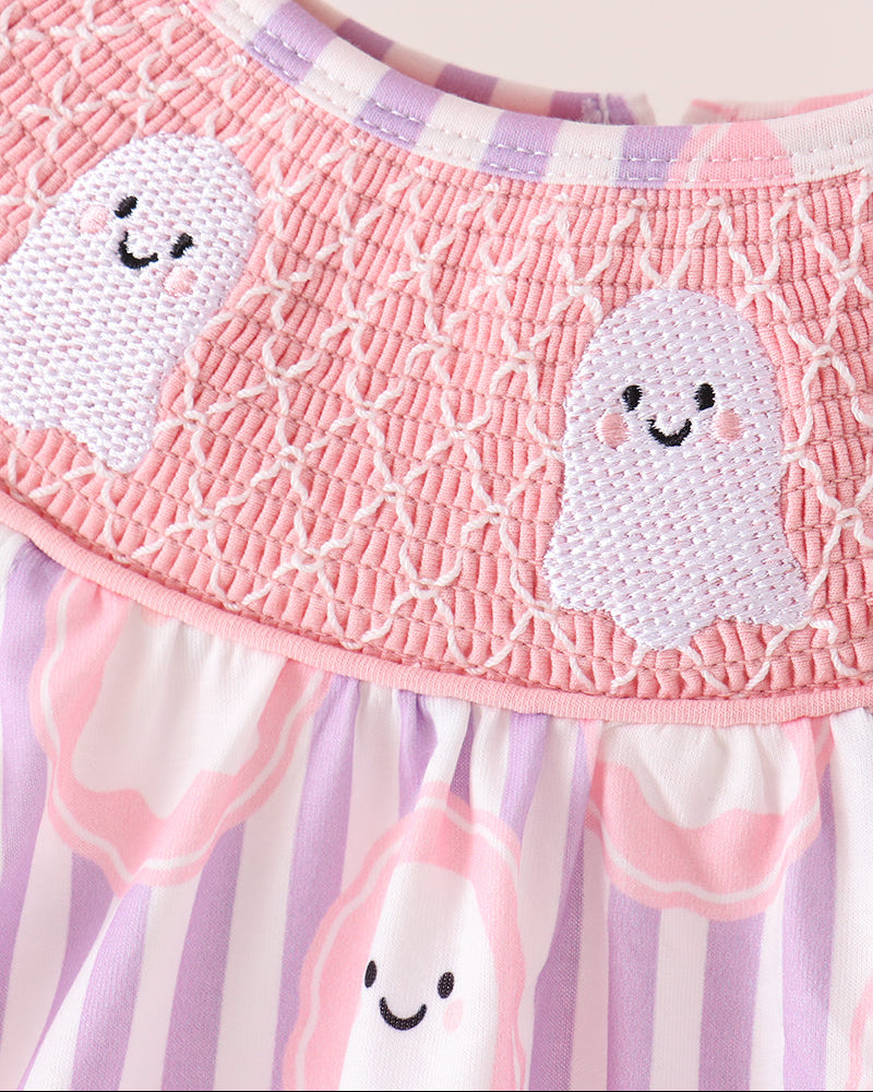 A close-up of a baby dress featuring a pink smocked bodice with embroidered smiling ghosts, a purple and white striped collar, and a matching purple and white striped skirt with pink ghost motifs.