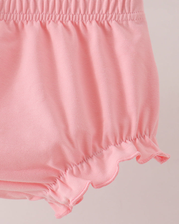 Close-up of a pair of light pink ruffled bloomers or shorts with an elastic waistband, shown against a plain light background.
