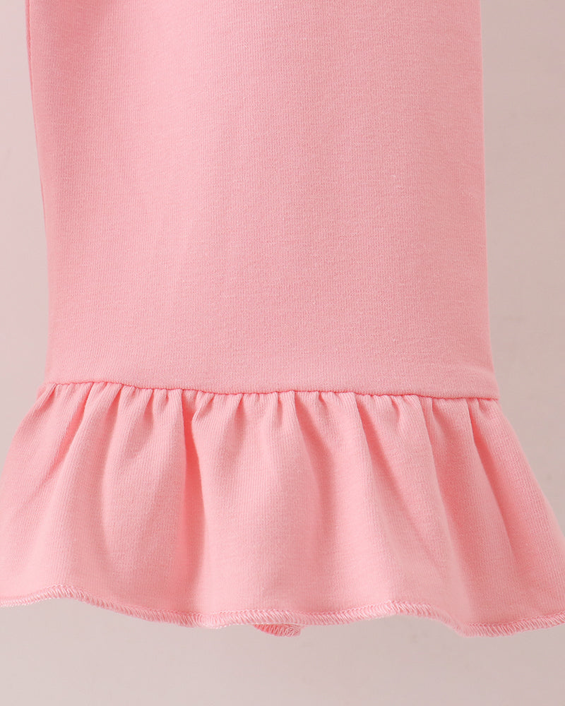 Close-up of a light pink garment with a ruffled hem, showing the fabric texture and construction against a plain light background.