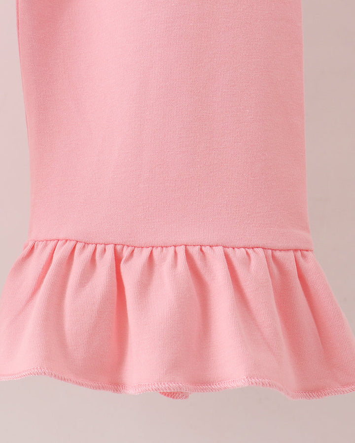 Close-up of a light pink garment with a ruffled hem, showing the fabric texture and construction against a plain light background.