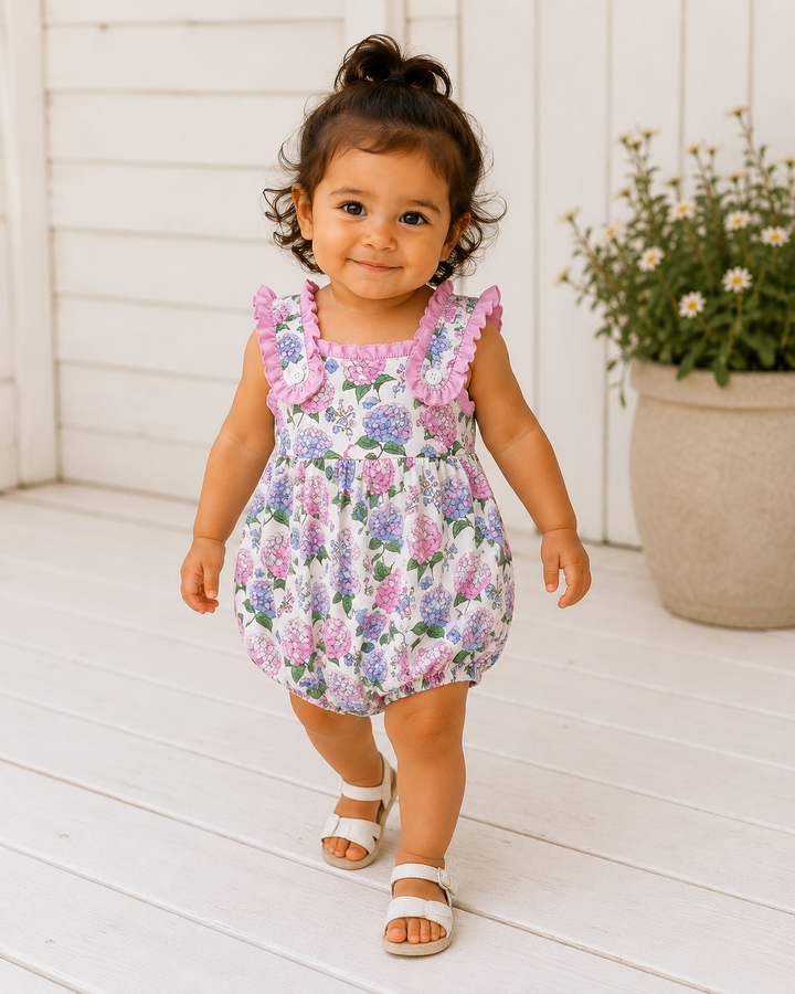 Child wearing a floral dress with pink ruffles on a white wooden floor.
