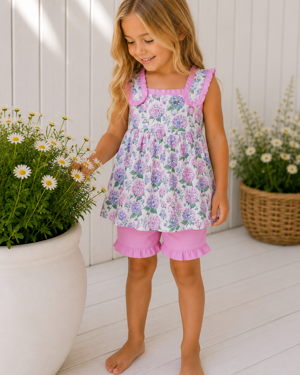 Young girl in a floral dress and pink shorts standing outdoors with plants around.